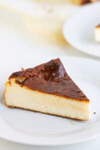 slice of burnt cheesecake on a white plate on a white surface